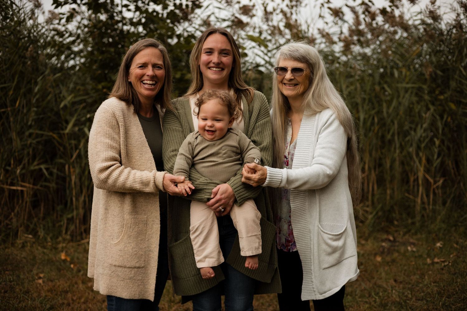 A group of people wearing neutral tones stand together outdoors during a fall photo session in nature.