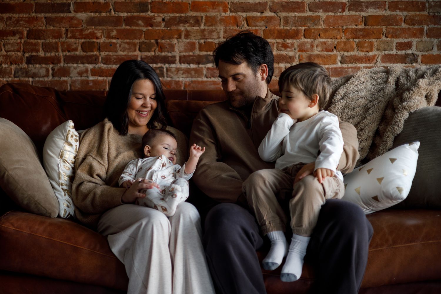 A series of intimate family moments with a newborn baby against exposed brick walls in a cozy home setting.