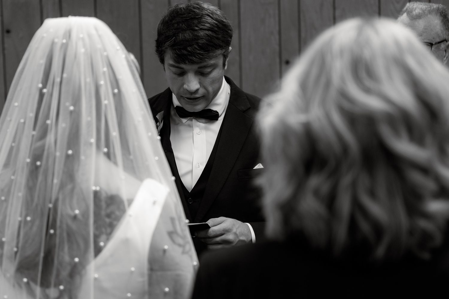 A black and white photograph shows a group of wedding guests gathered together in formal attire.