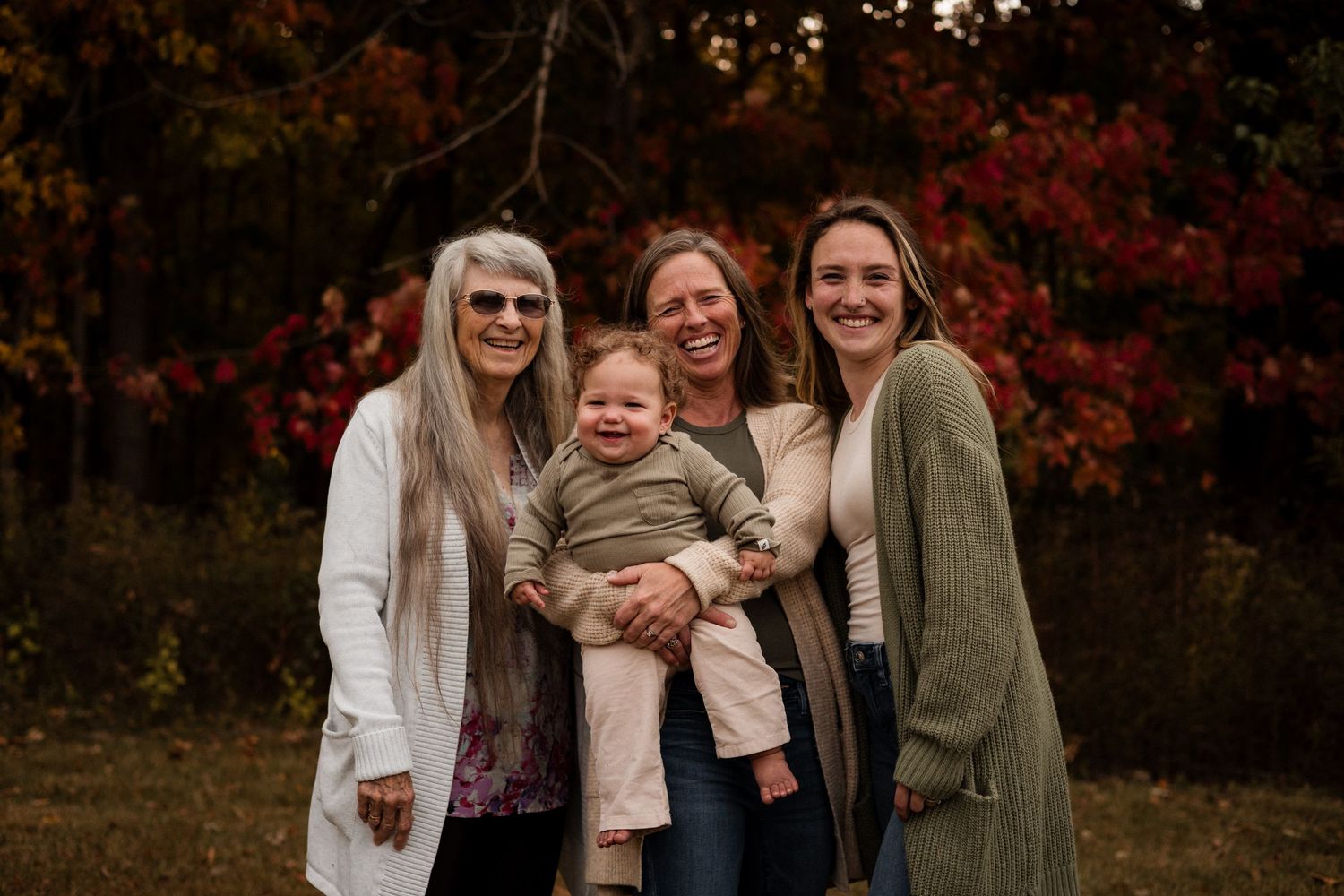 A family enjoys a warm autumn day together outdoors with vibrant red foliage in the background.