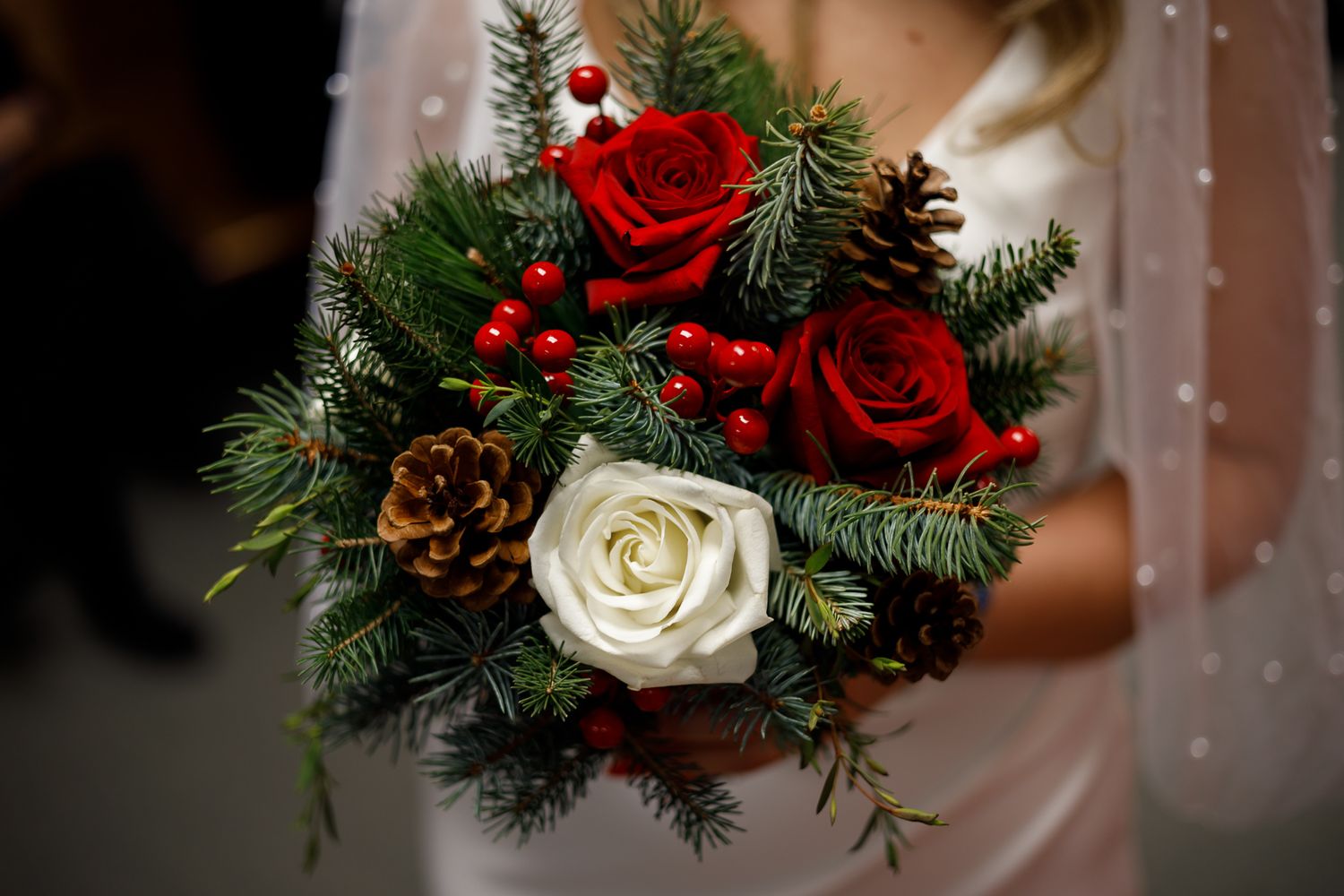 Festive holiday bouquet featuring red roses, white flowers, and evergreen pine branches with pinecones.