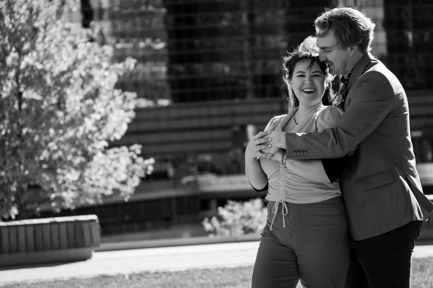 A romantic black and white moment captured outdoors with a couple embracing and laughing together.