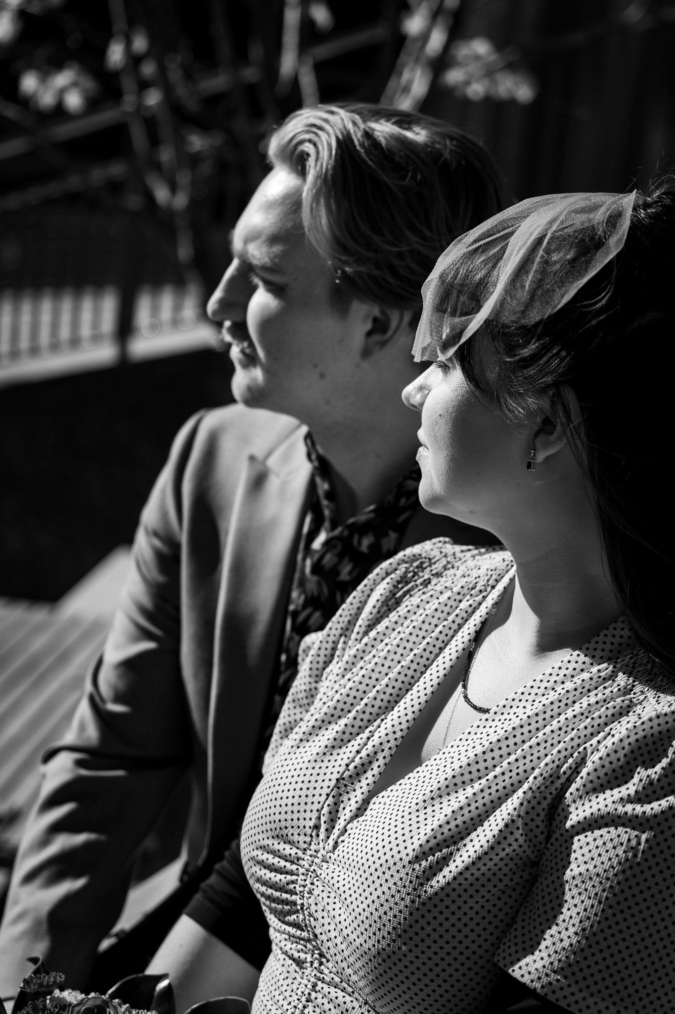 A black and white photograph of a couple in vintage 1950s clothing sitting together in profile view.