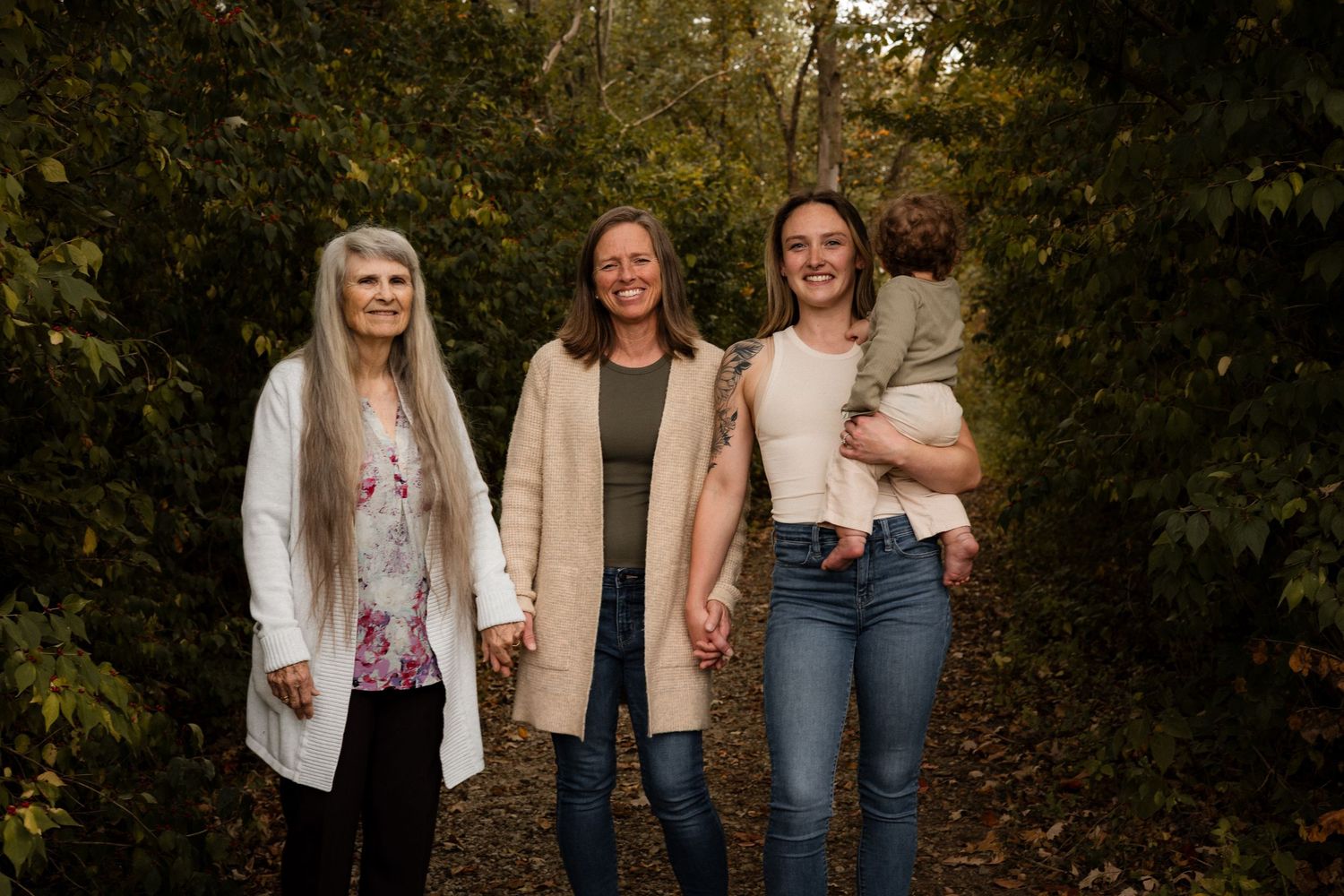 A group stands together outdoors on an autumn day with fallen leaves and trees in the background.