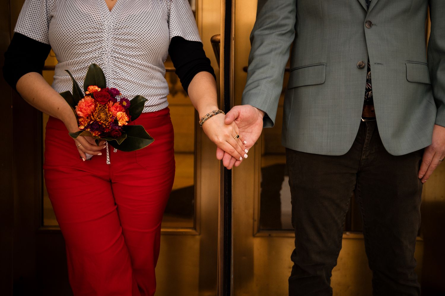 Close-up detail of someone wearing red pants and a gray blazer while standing indoors.