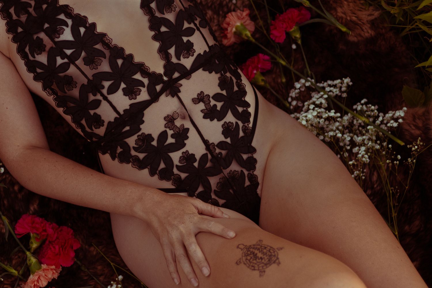 Close-up view of a delicate floral lace pattern against skin with a small decorative tattoo visible.