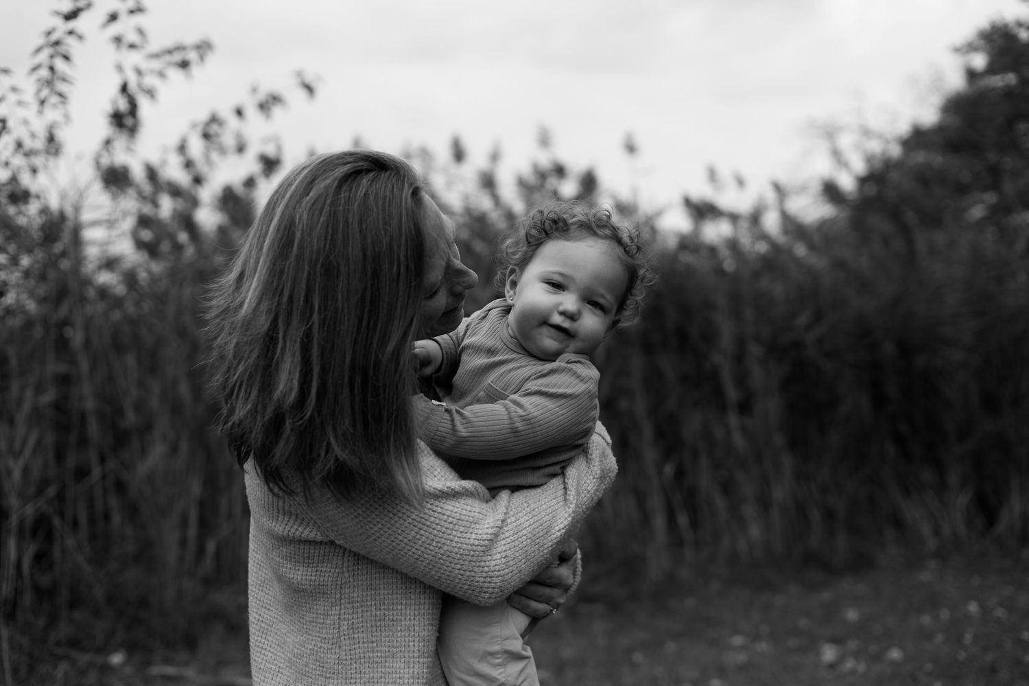A black and white photograph shows a tender moment between a parent and child embracing outdoors in a natural setting.