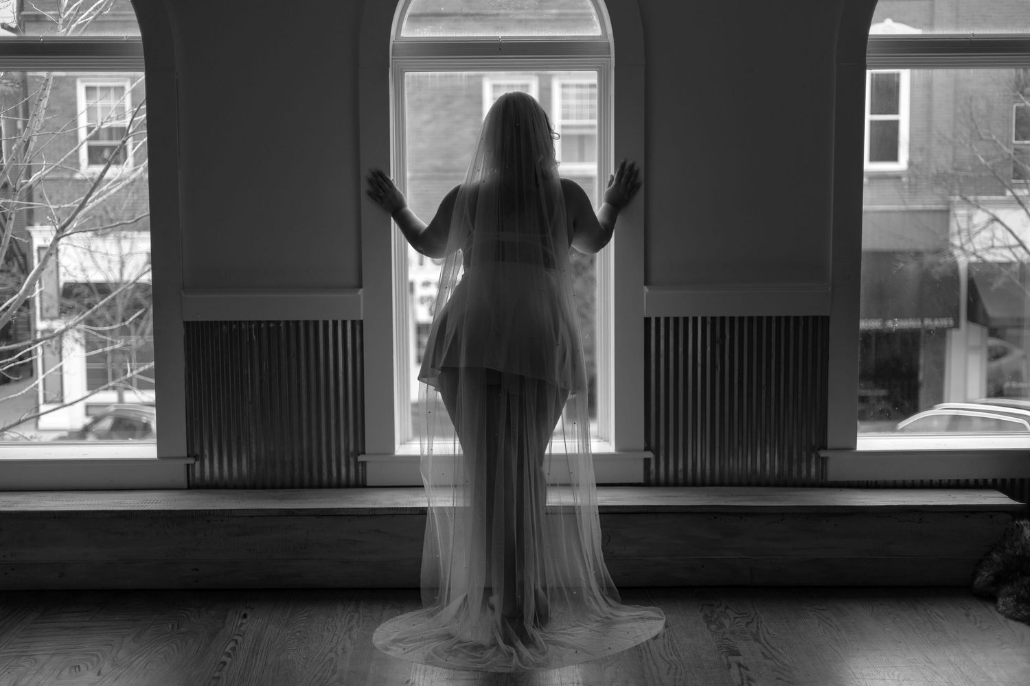 A series of silhouetted figures stand in front of bright windows in a dark interior space creating a moody atmosphere.