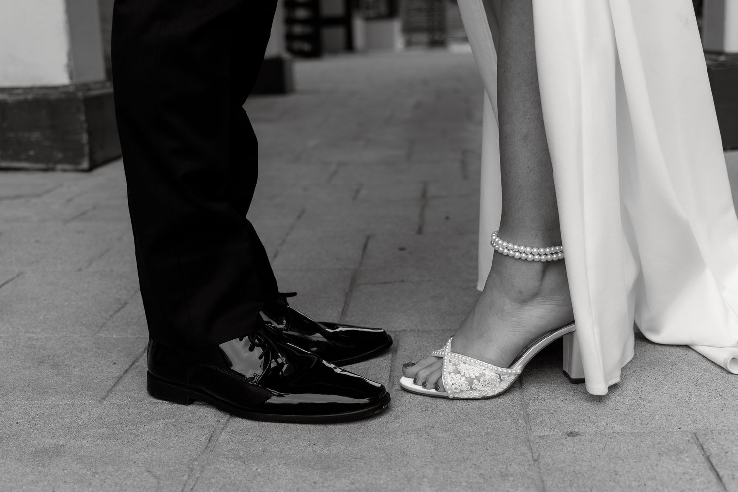 Black and white wedding photo showing bride and groom's feet dancing together on a stone floor.