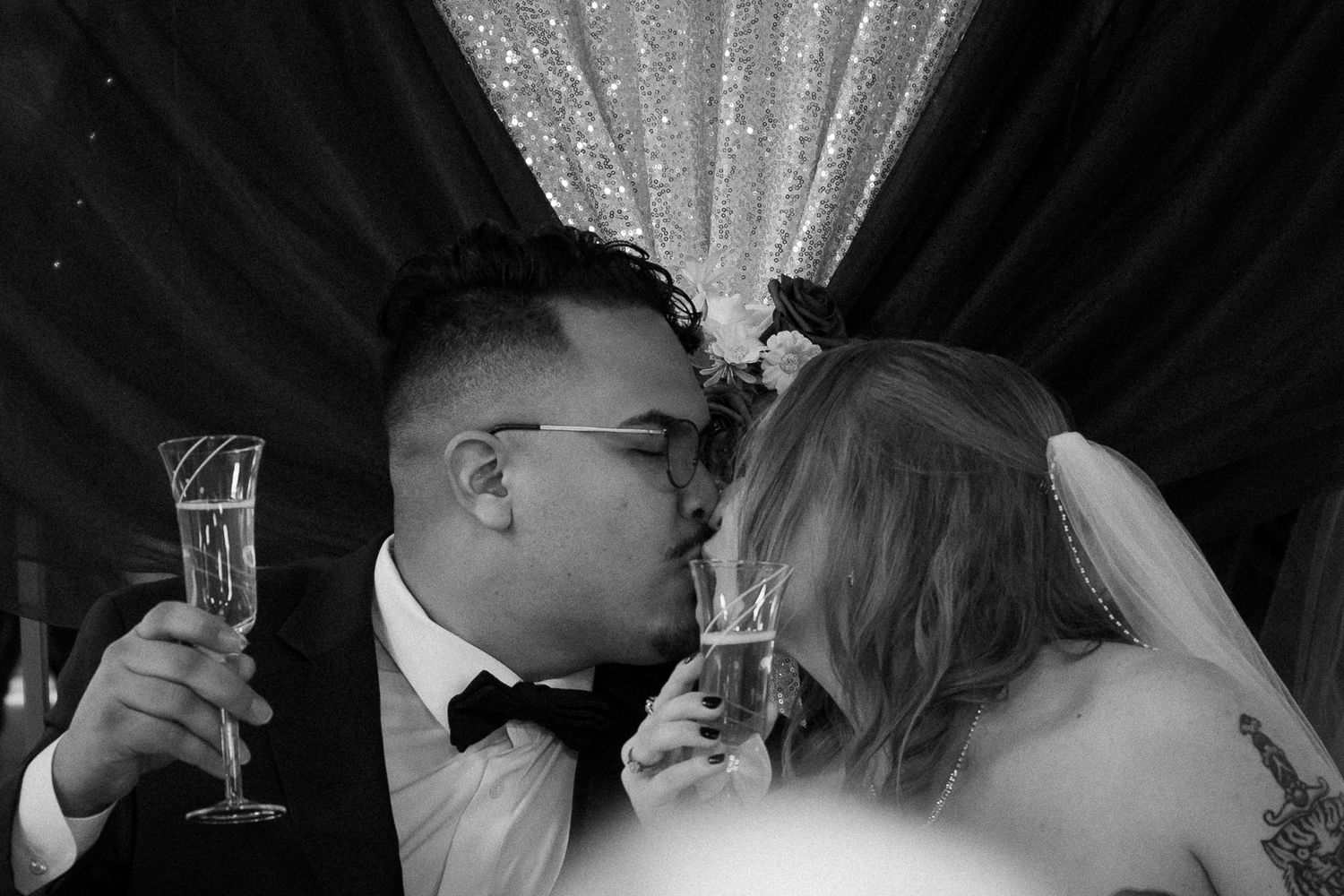 A romantic couple shares a tender kiss at their wedding reception while holding champagne glasses in an elegant venue.