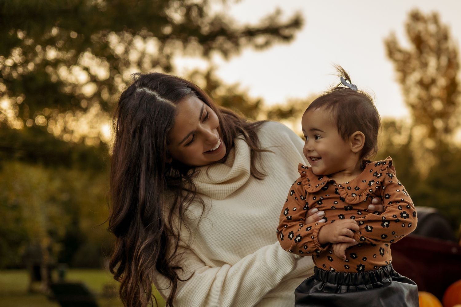 A loving family moment captured during golden hour in a park with warm autumn sunlight filtering through the trees.