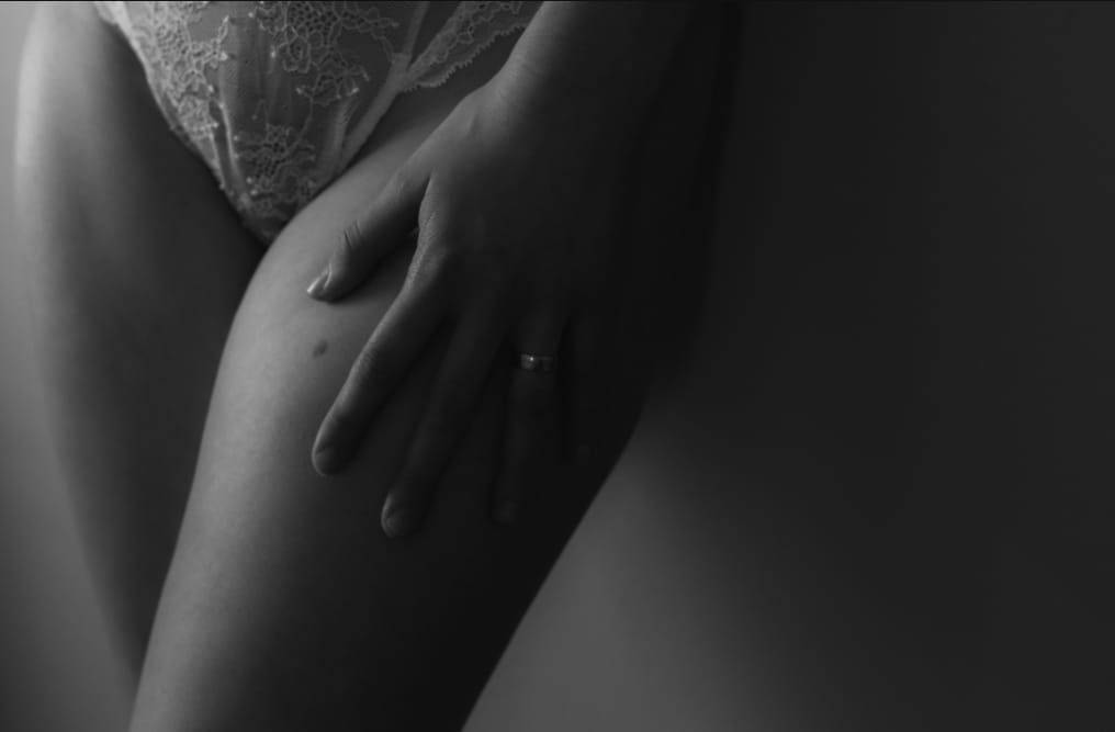 Black and white artistic close-up photograph of a hand resting on bare skin in dramatic lighting.