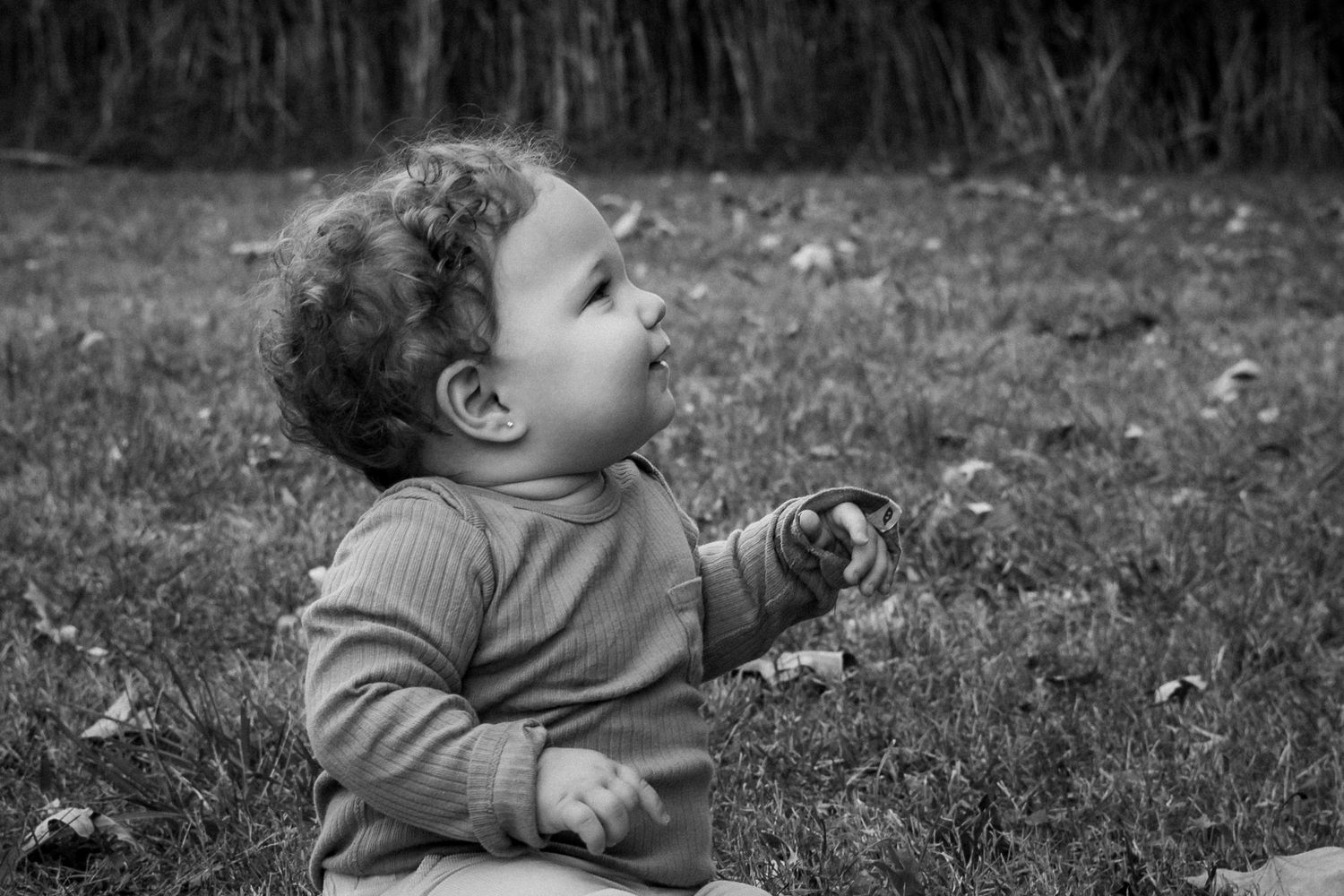 A sequence of black and white photographs showing a child playing and looking up while sitting in grass outdoors.