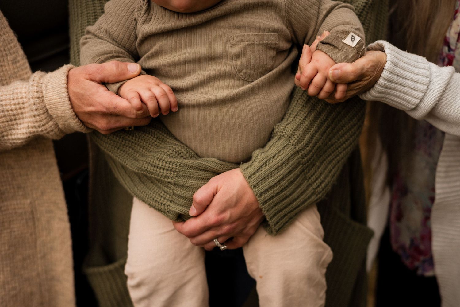 Hands gently support someone wearing a beige shirt and olive green sweater while sitting.