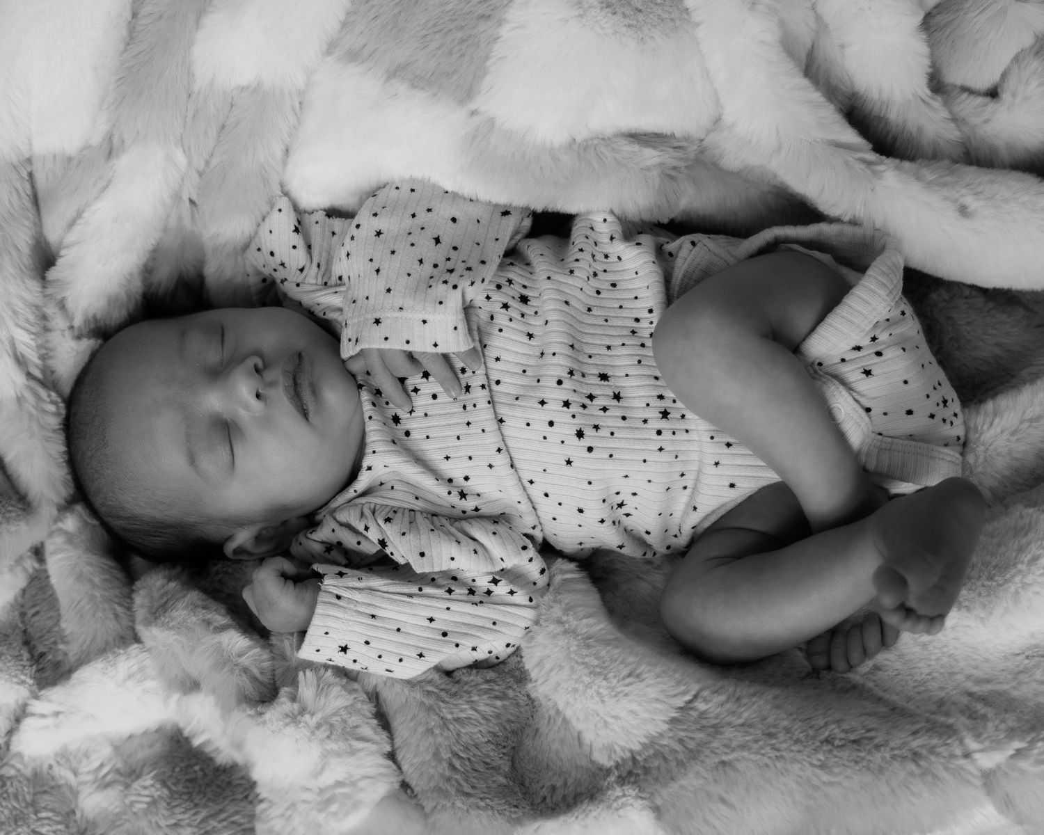 A sleeping newborn baby wrapped in a polka dot blanket lies peacefully on a soft surface.