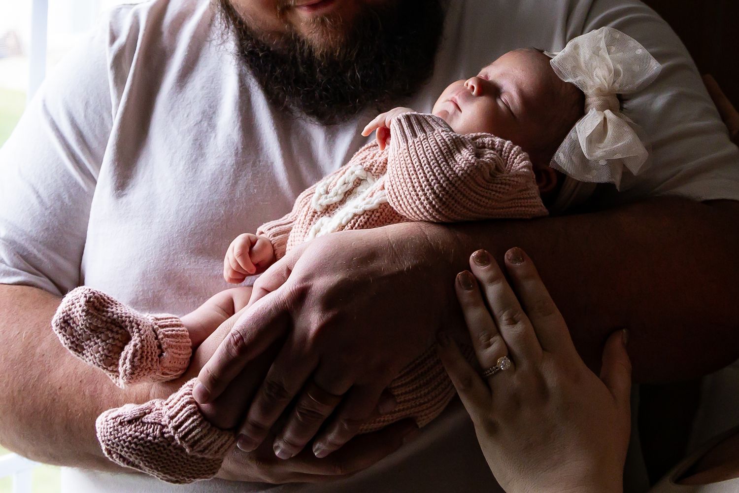 A newborn baby wearing pink knit booties rests in someone's arms.