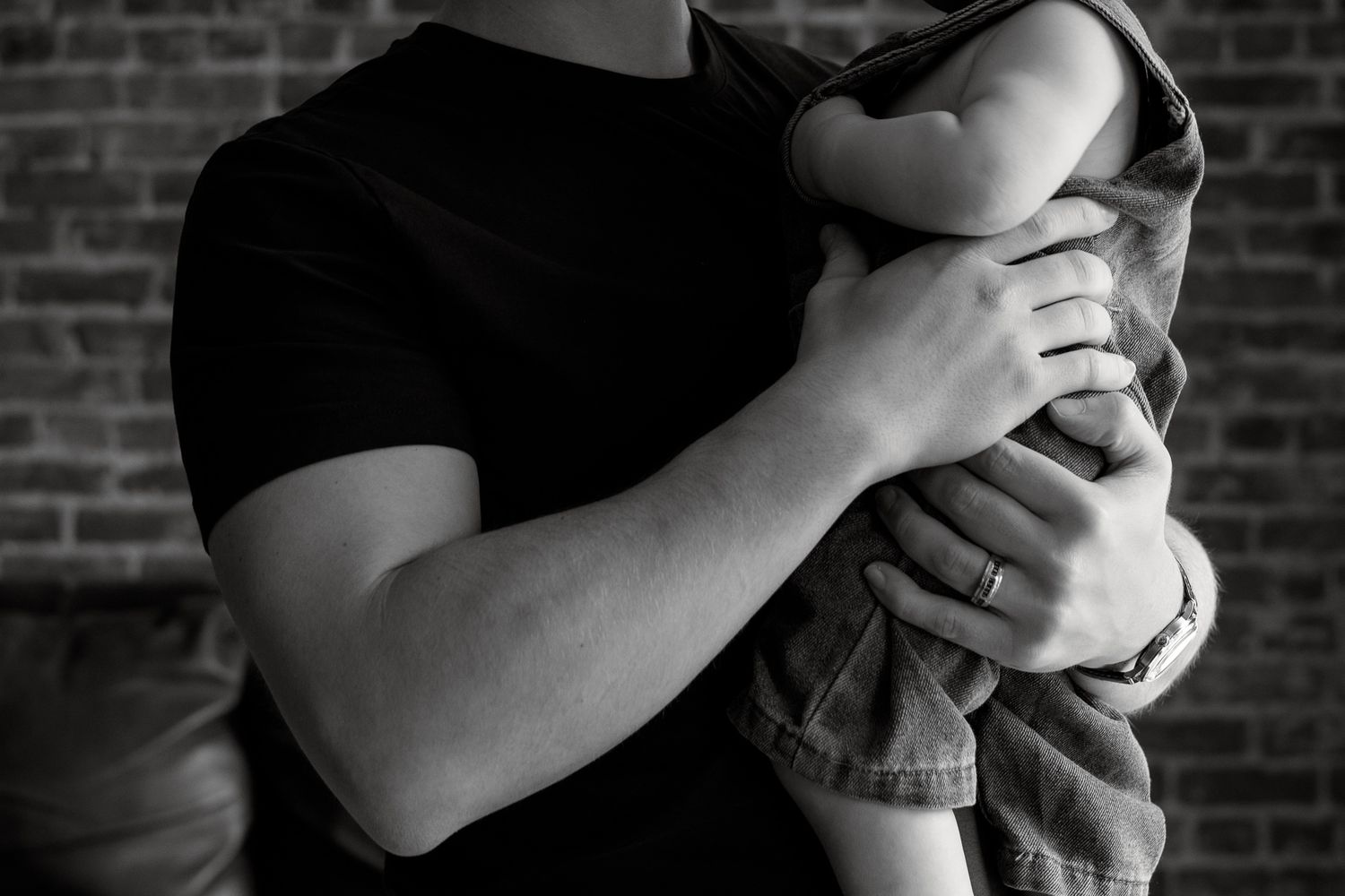 Black and white photo of a person in a black t-shirt tenderly holding a baby close to their chest.