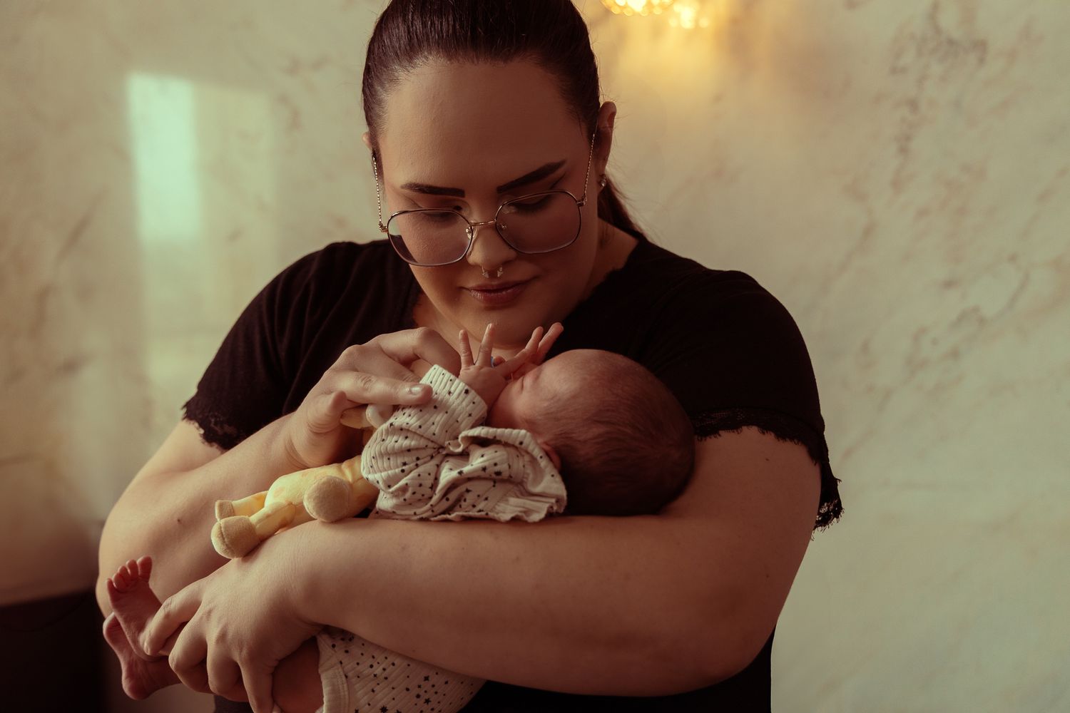 A tender moment captured as a mother in a black shirt holds and gazes lovingly at her sleeping newborn baby.