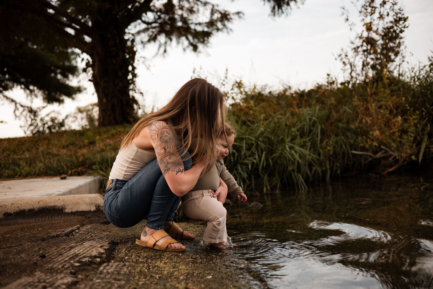 A couple sits on rocks by a serene lake during golden hour, creating a peaceful outdoor scene.