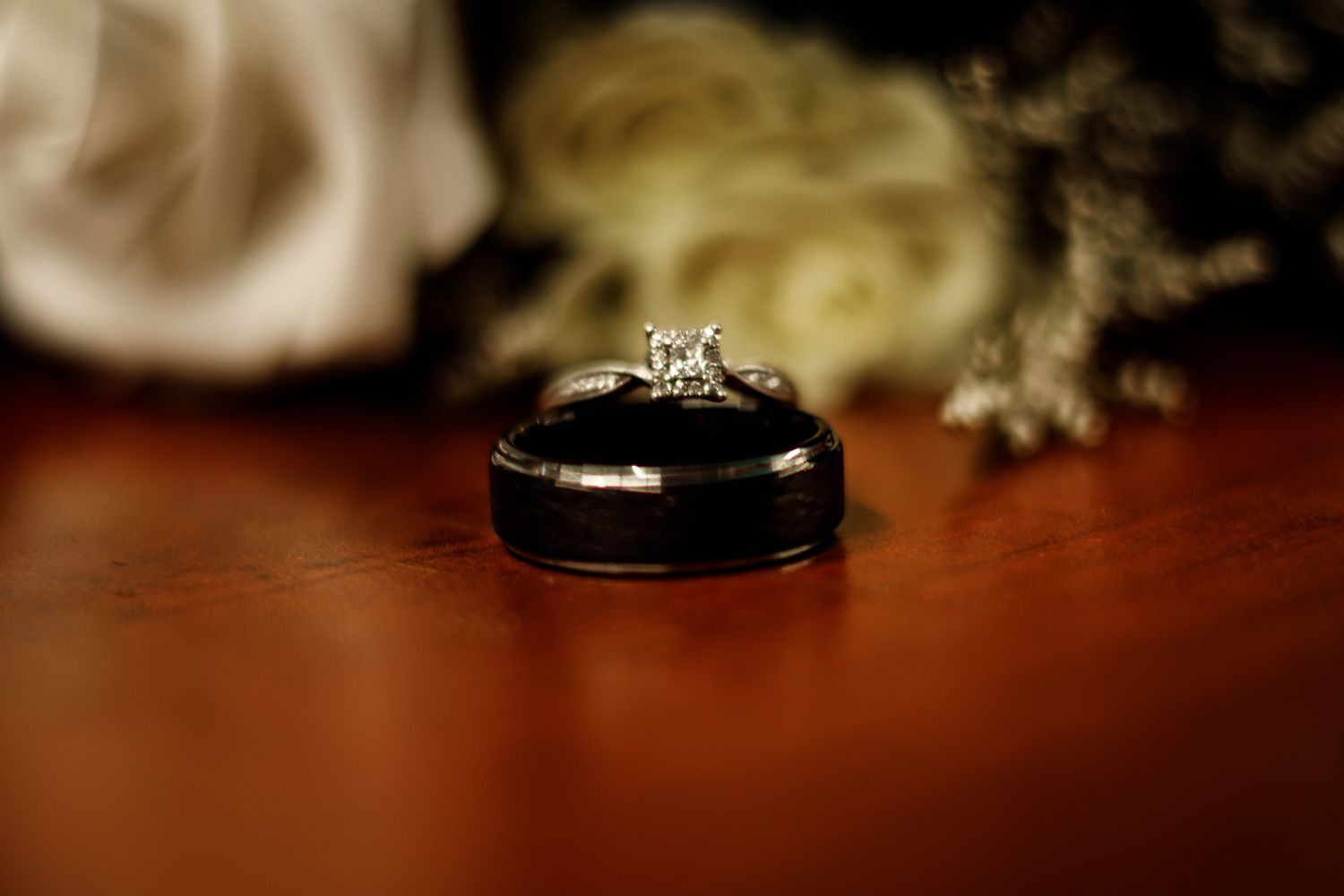 A silver wedding ring sits on a dark wooden surface with soft lighting and shallow depth of field.