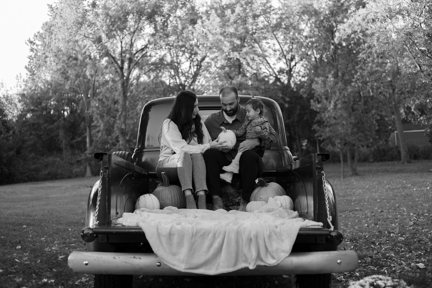 A romantic black and white photo showing a couple sitting in the back of a vintage pickup truck with a draped blanket.