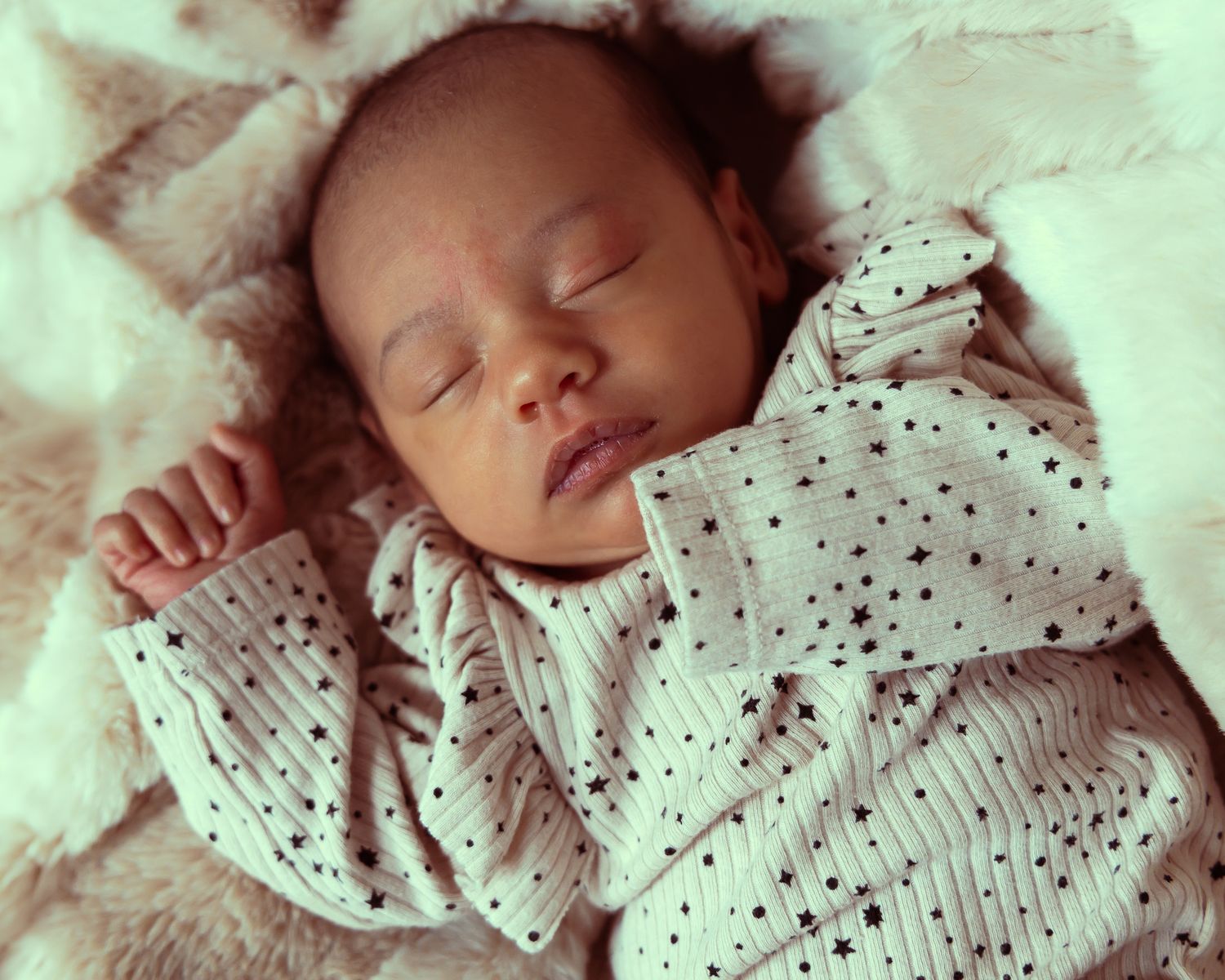 Sleeping baby in white polka dot outfit rests peacefully on soft white bedding.