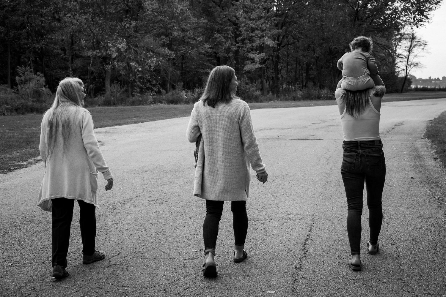 Three people walking away on a path wearing casual coats and pants in black and white photography.
