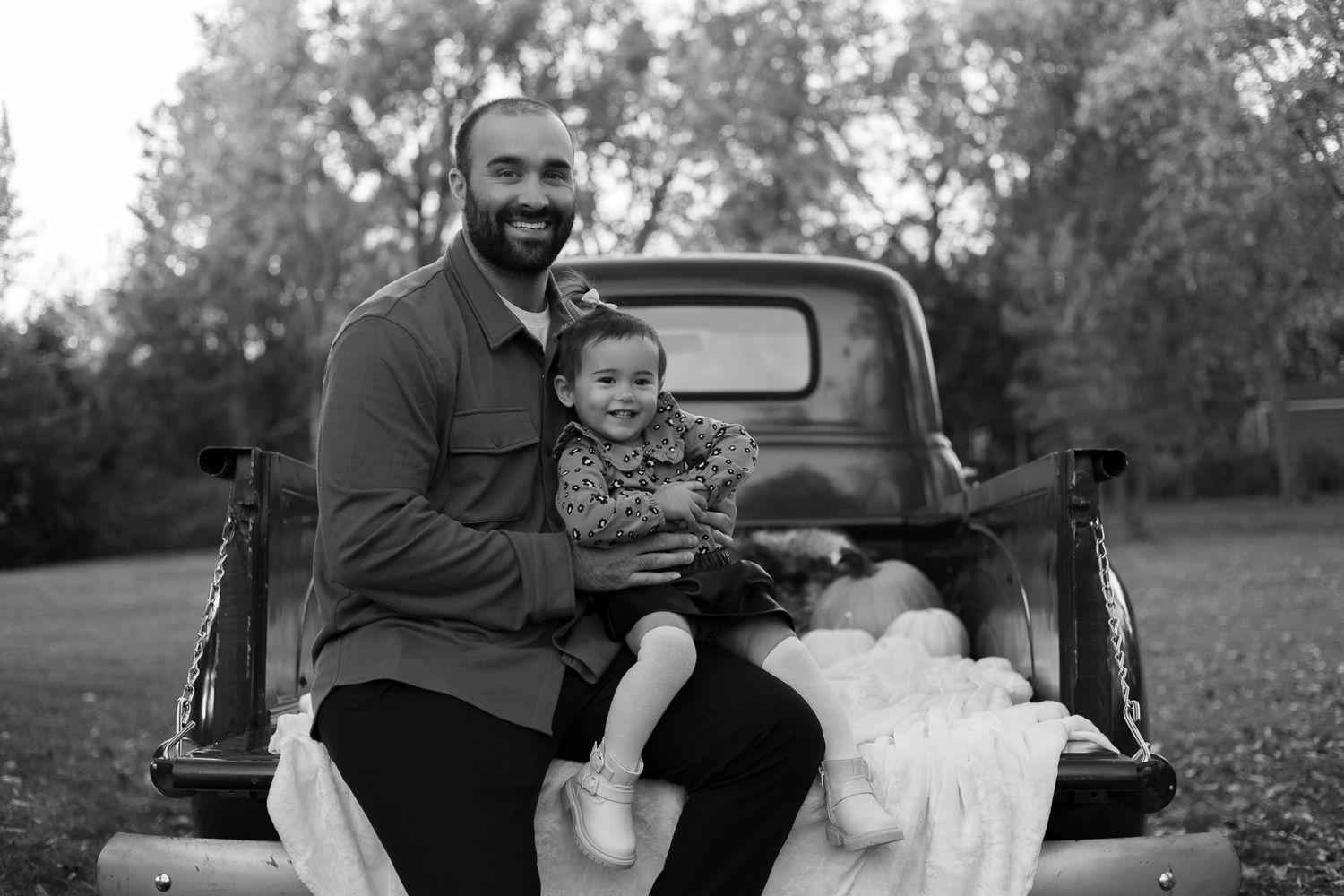 Black and white photo of a parent and child sitting together in the bed of a vintage pickup truck.