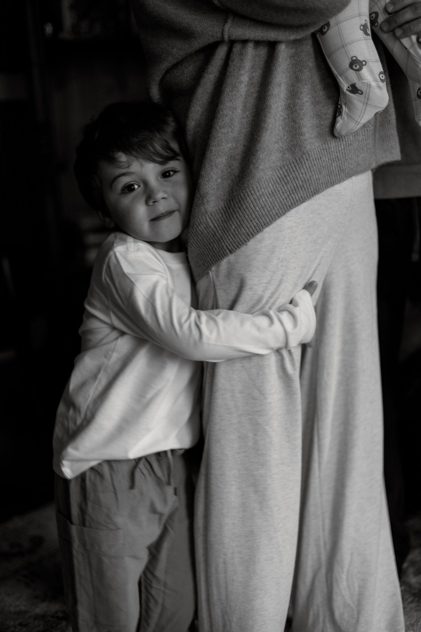 Black and white image sequence showing a child in white shirt hugging an adult's legs in a tender moment.