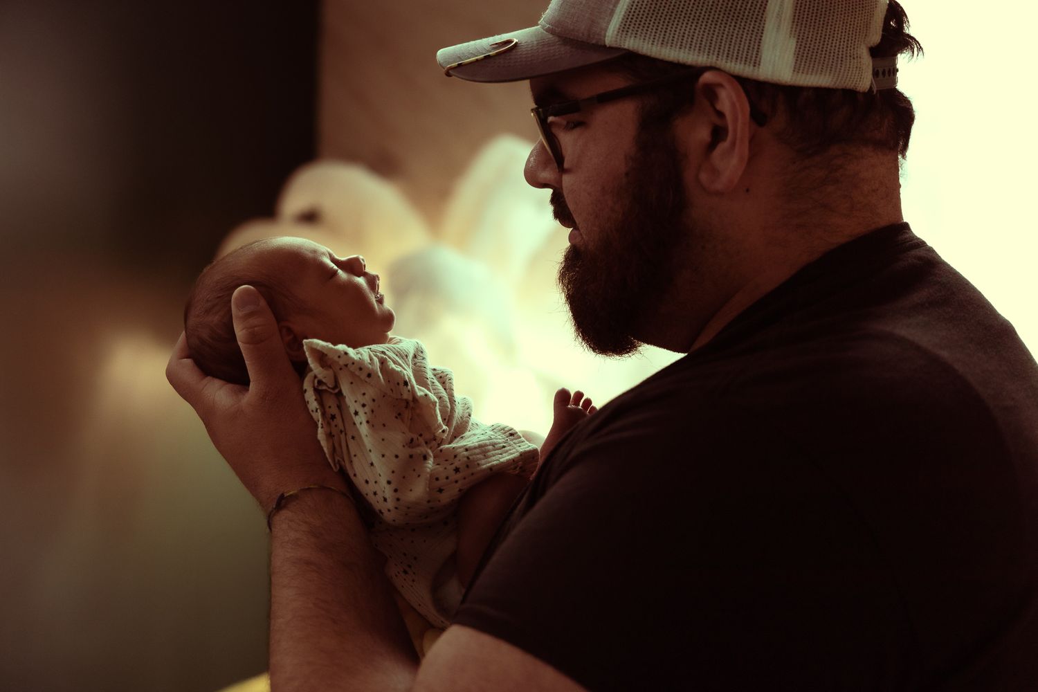 Person in a baseball cap and glasses examines a glass container in warm lighting.