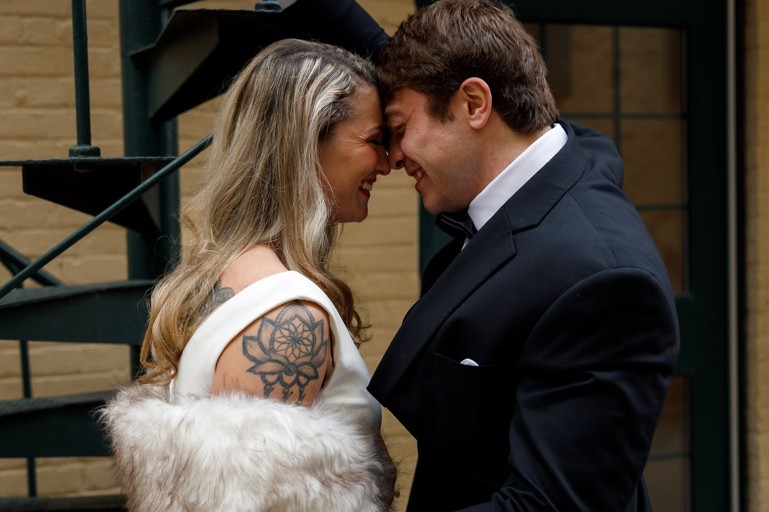 A couple shares an intimate moment at their wedding, with the bride wearing a white dress showing her arm tattoo.