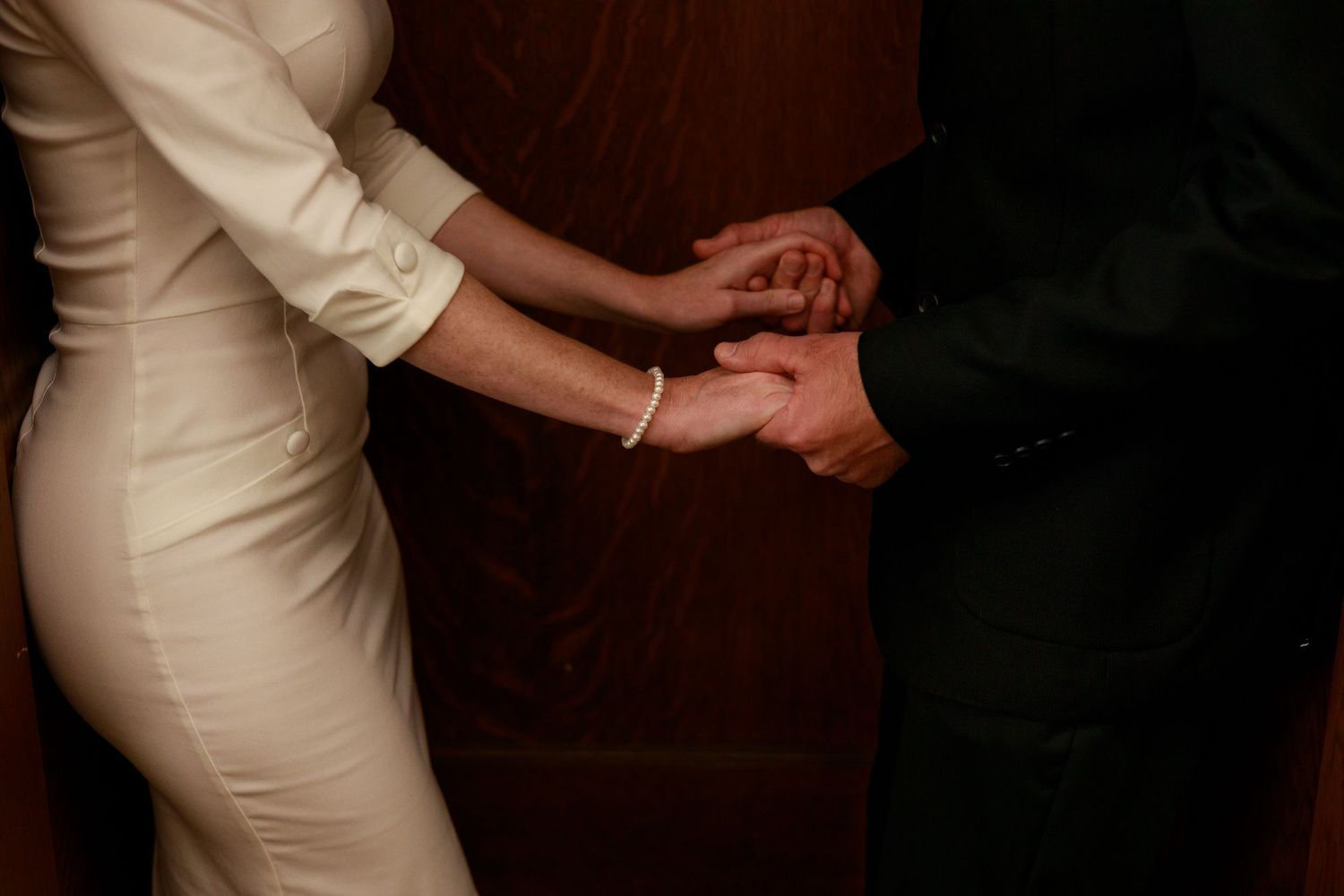 Two people hold hands intimately in a romantic moment, with one wearing an elegant white dress.