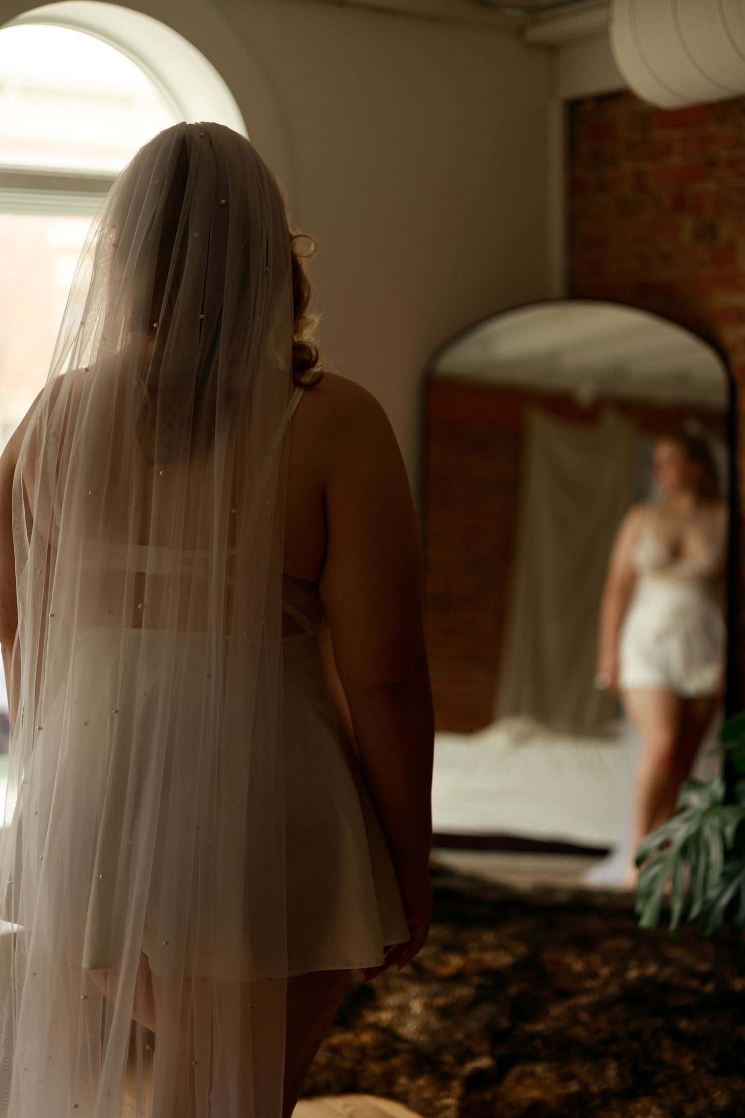 Bridal boudoir photo with flowing veil in front of arched doorway.