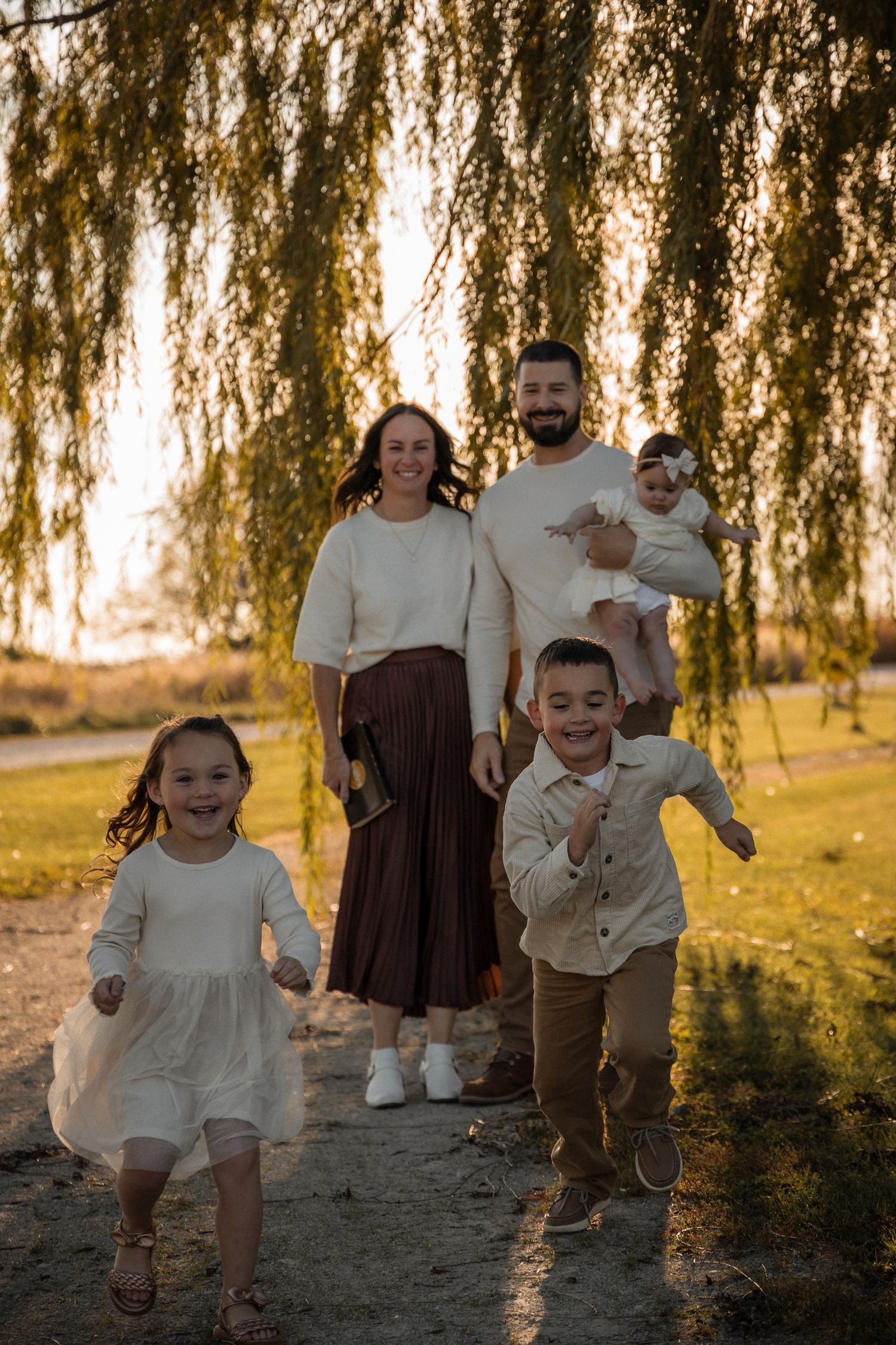 A family poses together under a weeping willow tree at sunset with golden light filtering through the branches.