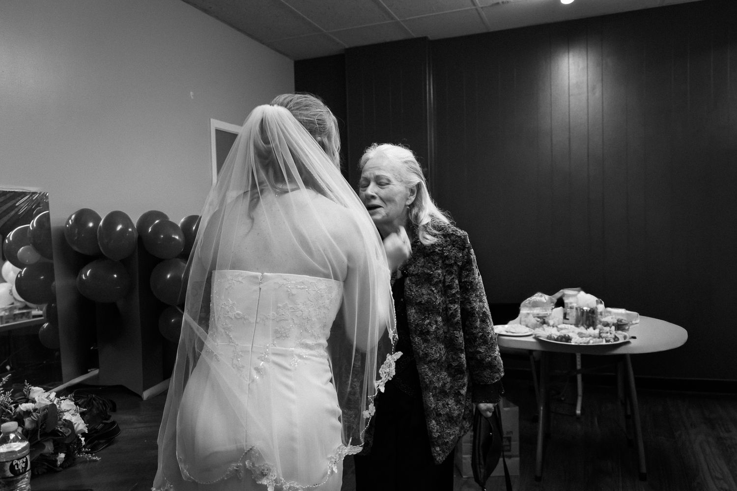 A black and white candid moment captured in a bridal preparation room showing two people in conversation.