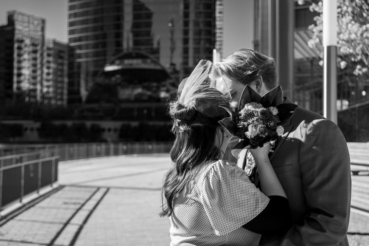 A black and white romantic moment captured on an urban balcony with city buildings in the background.