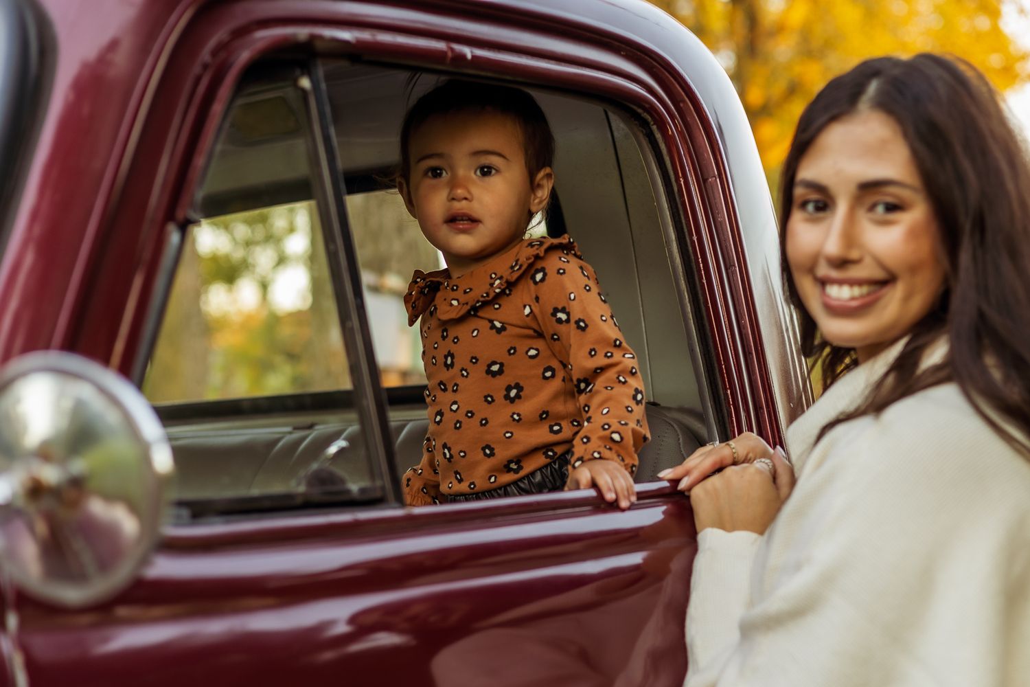 A group of passengers sit inside a vintage burgundy car with yellow autumn trees visible through the windows.