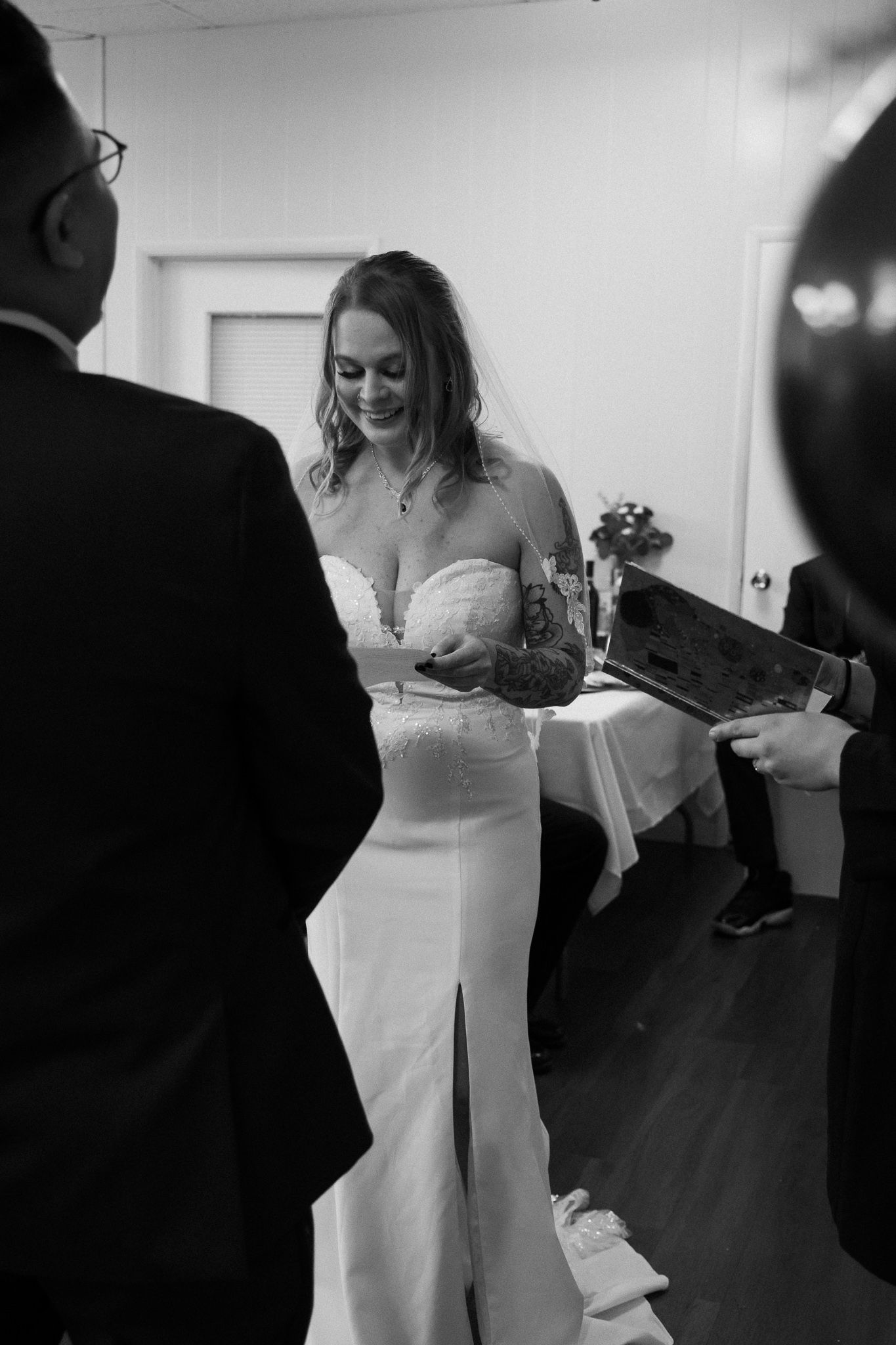 A bride in a white off-shoulder wedding dress dances with guests at a wedding reception in black and white.