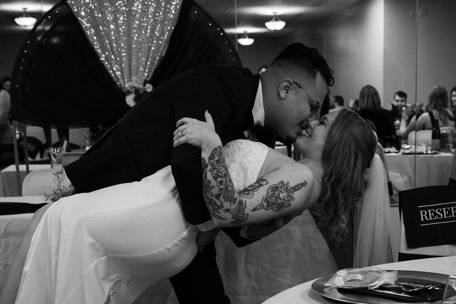 A romantic black and white photo of a couple sharing a passionate kiss during their wedding reception.