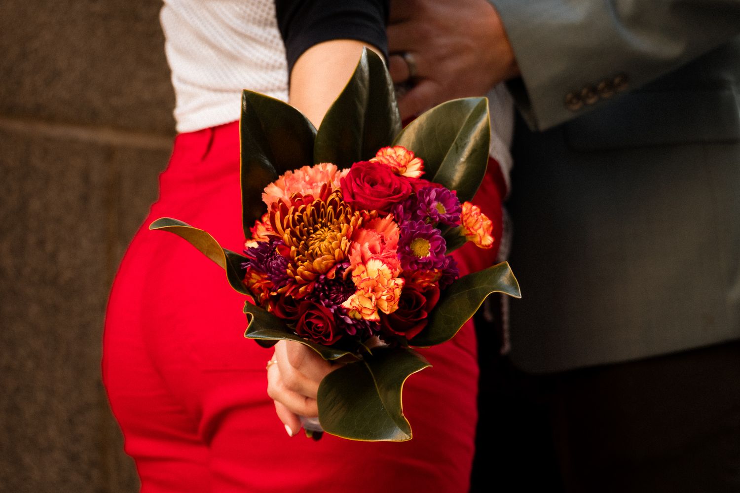 Close-up view of vibrant red and orange wedding bouquet with mixed flowers against dark background.