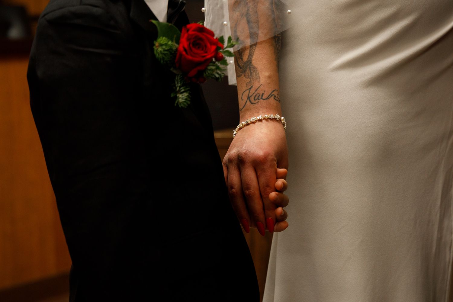 Close-up detail shot of hands holding a wedding bouquet with white roses and greenery against a white dress.