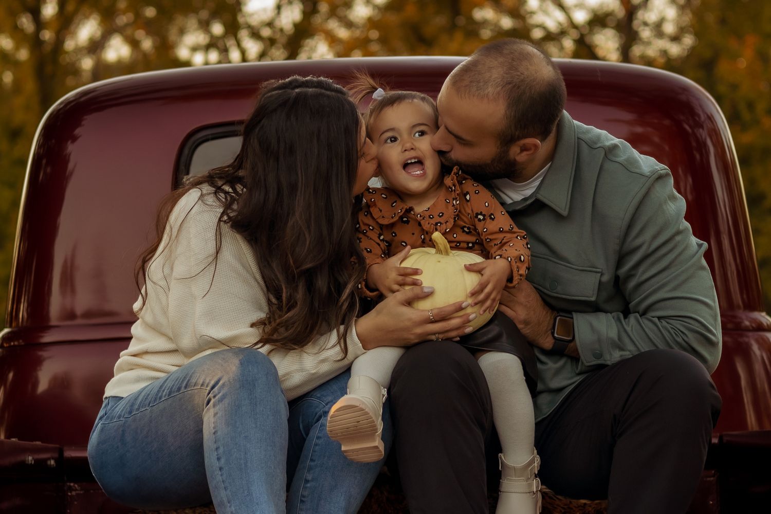 Family shares joyful moments together while sitting in the back of a vintage red pickup truck at sunset.