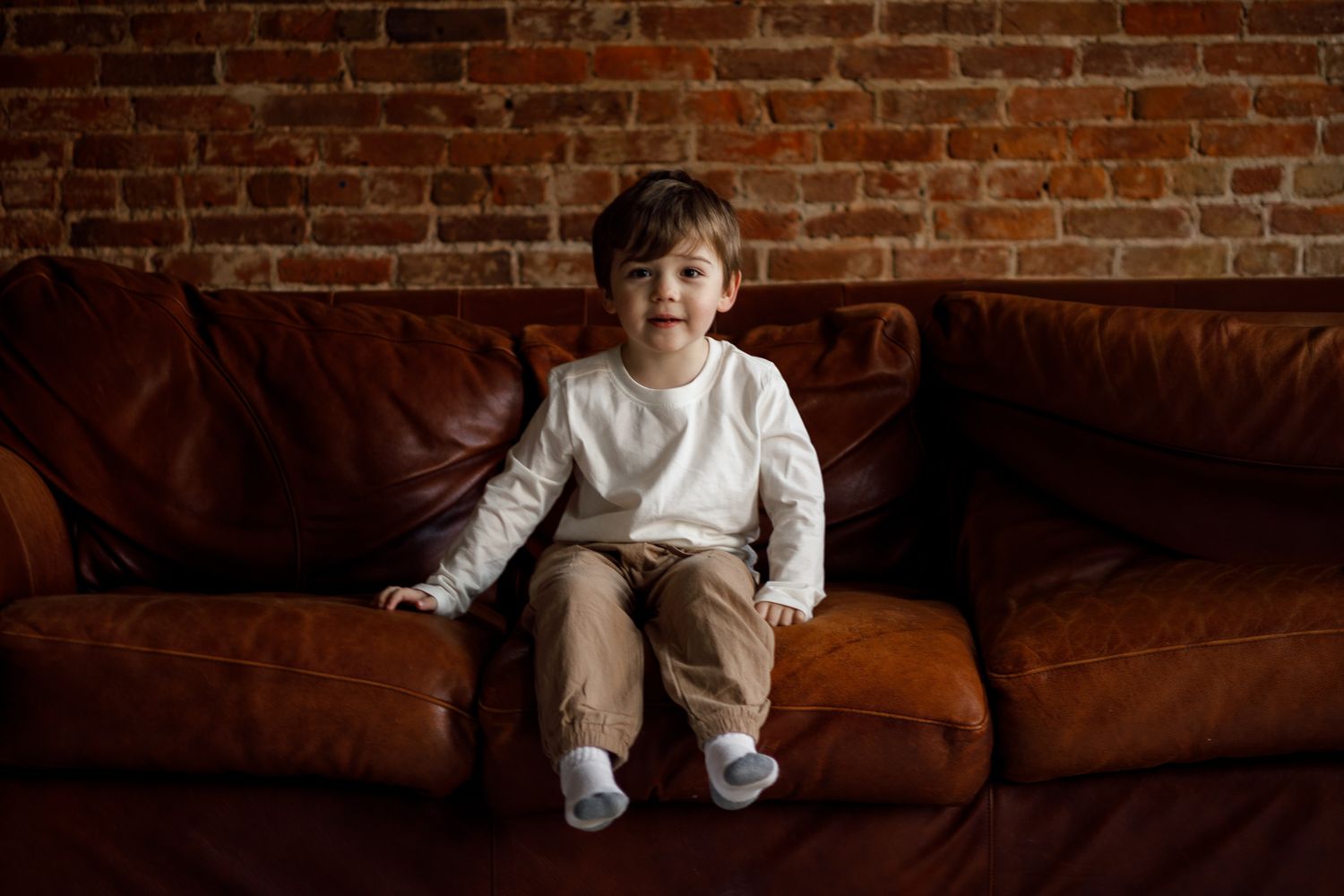 A series of connected images showing a child in white clothing playing on a dark brown leather couch.