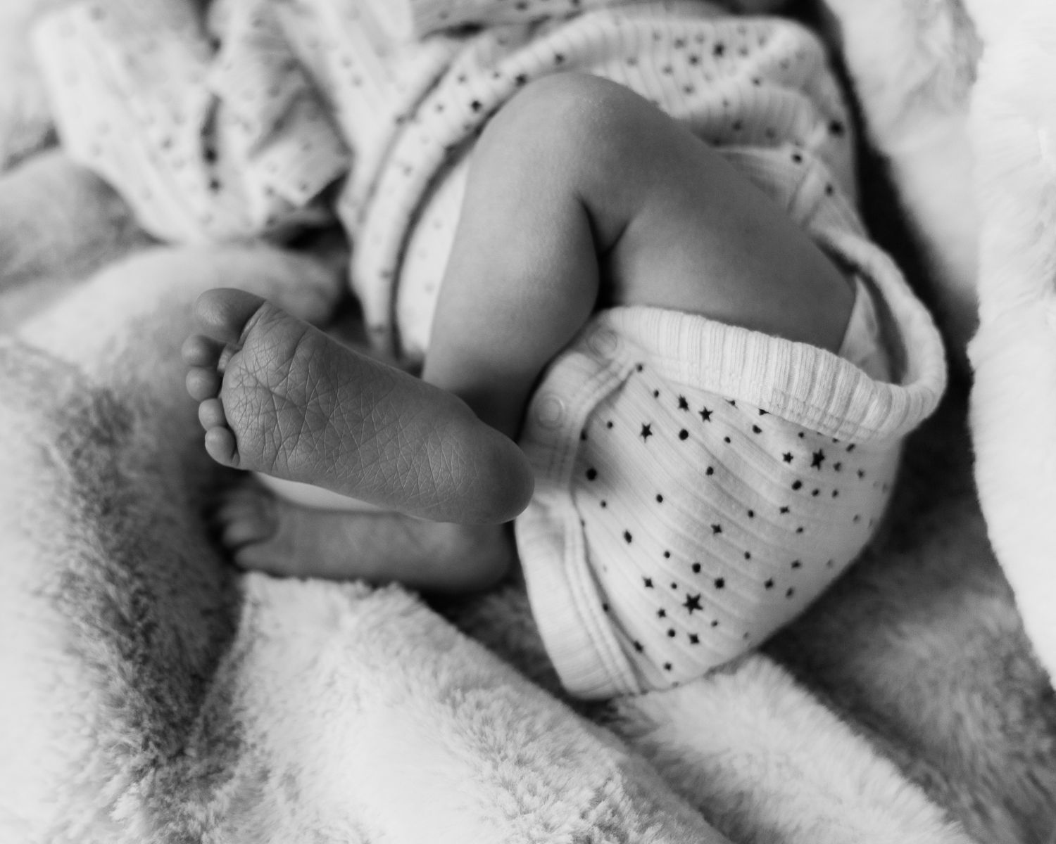Close-up black and white photo of tiny baby feet wearing polka dot socks while resting on soft blanket.