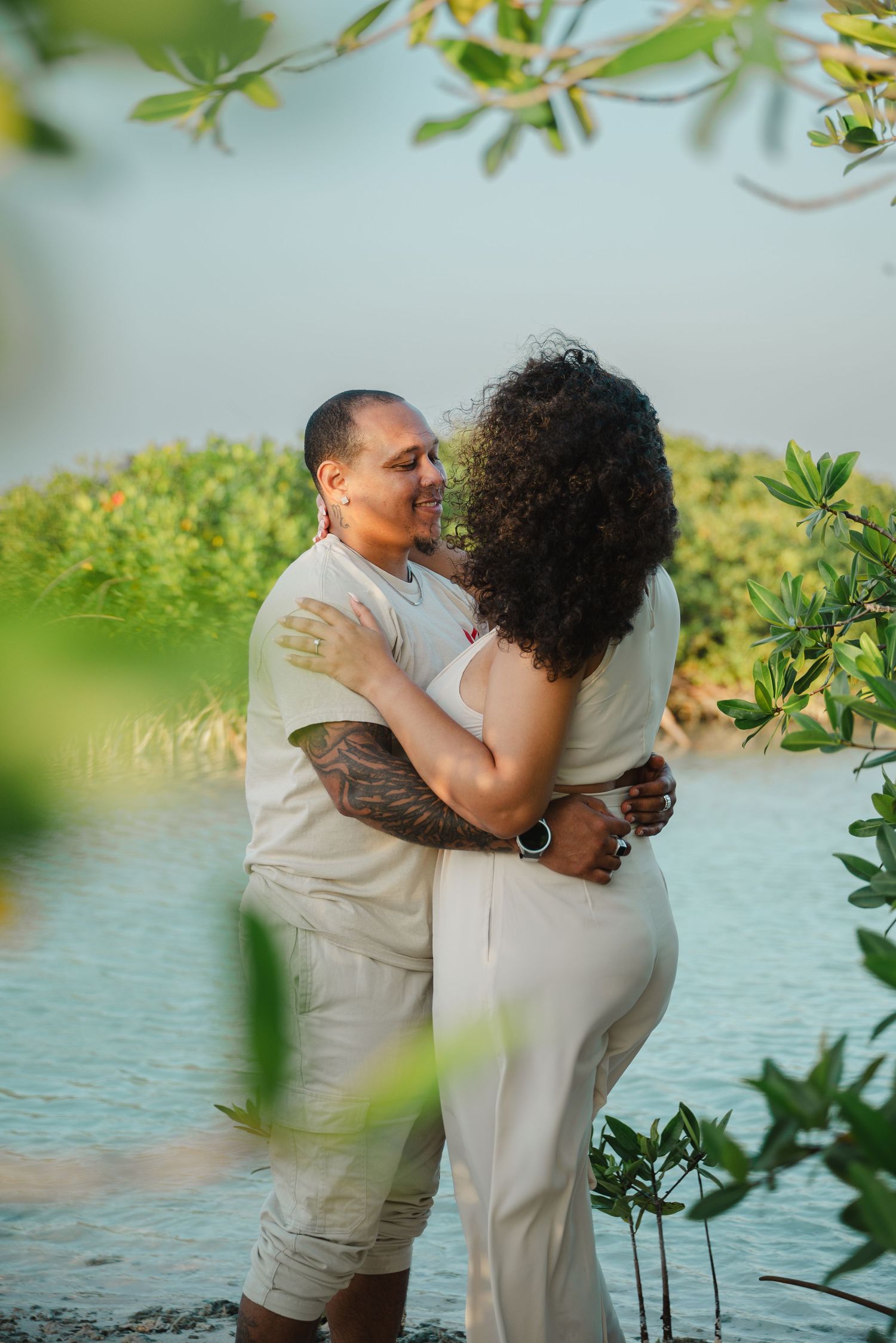 Couple sharing a kiss while embracing near tropical mangrove waterway at dusk.