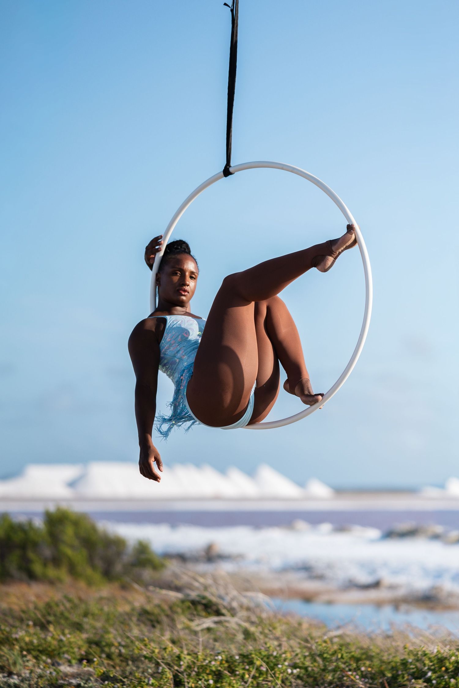 Aerial acrobat performing in a hoop over coastal landscape.