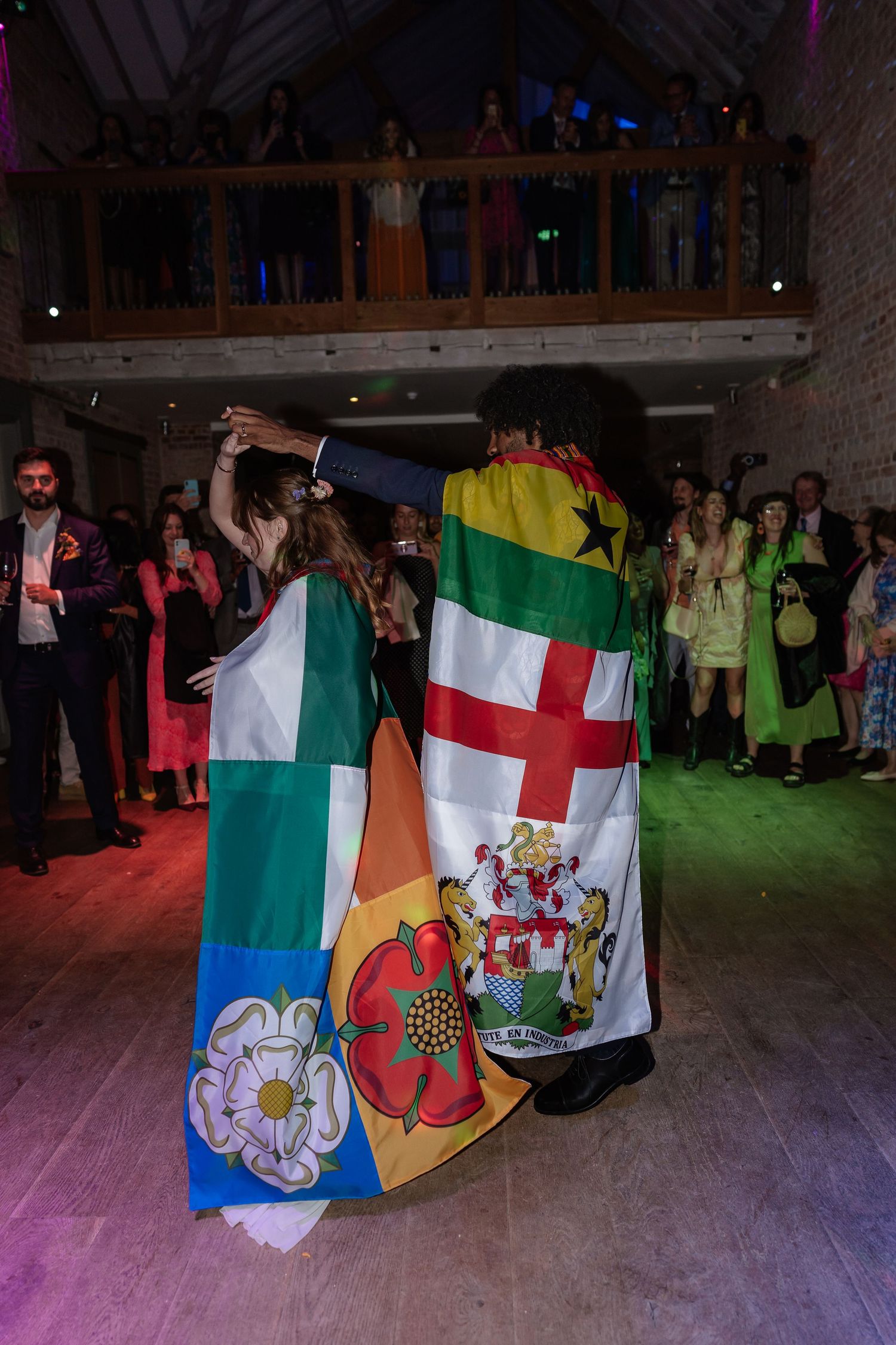 Couple dancing wrapped in flags of multiple nations at lively wedding reception.