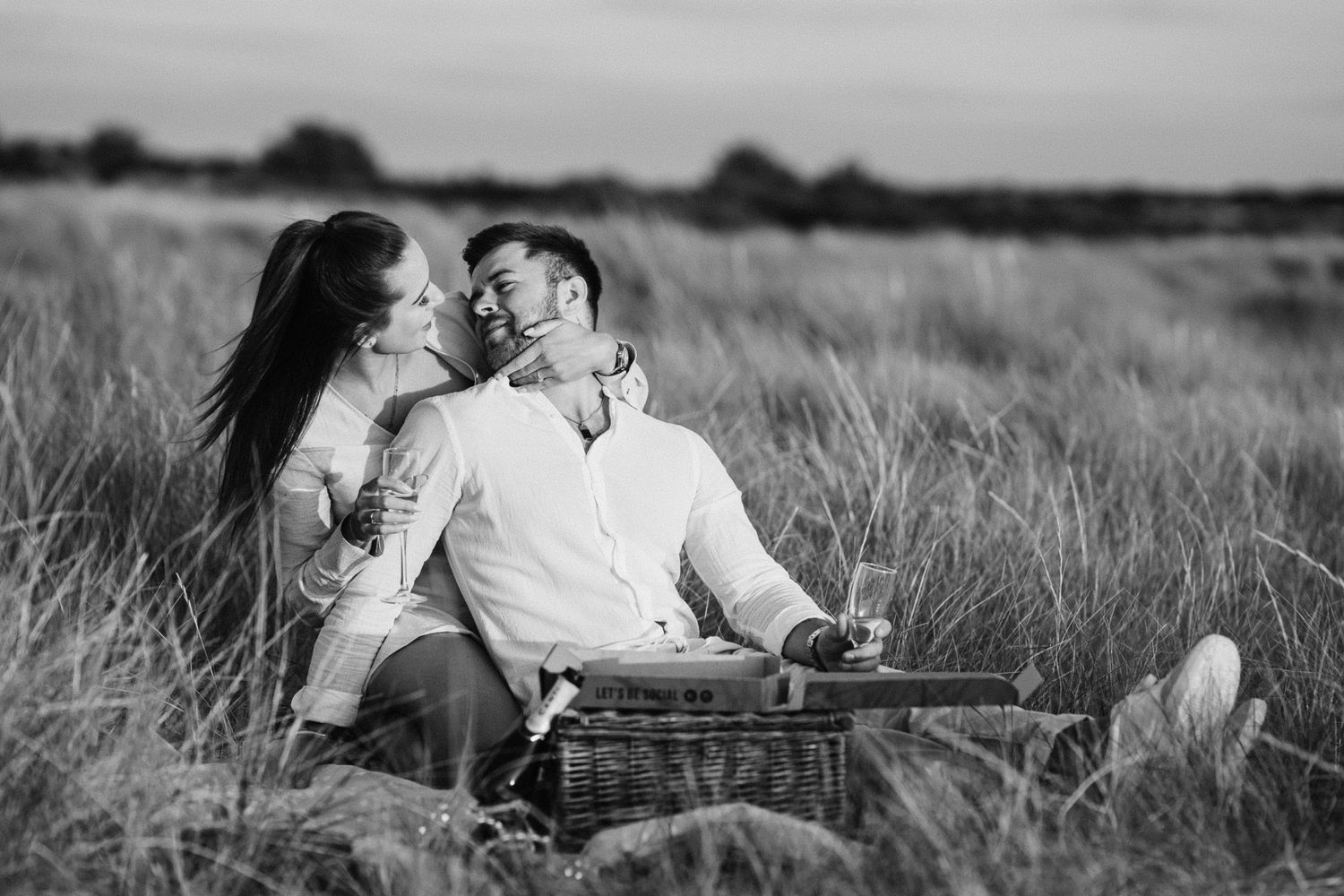 Black and white photo of a loving couple sharing an intimate moment during a picnic in a grassy field.