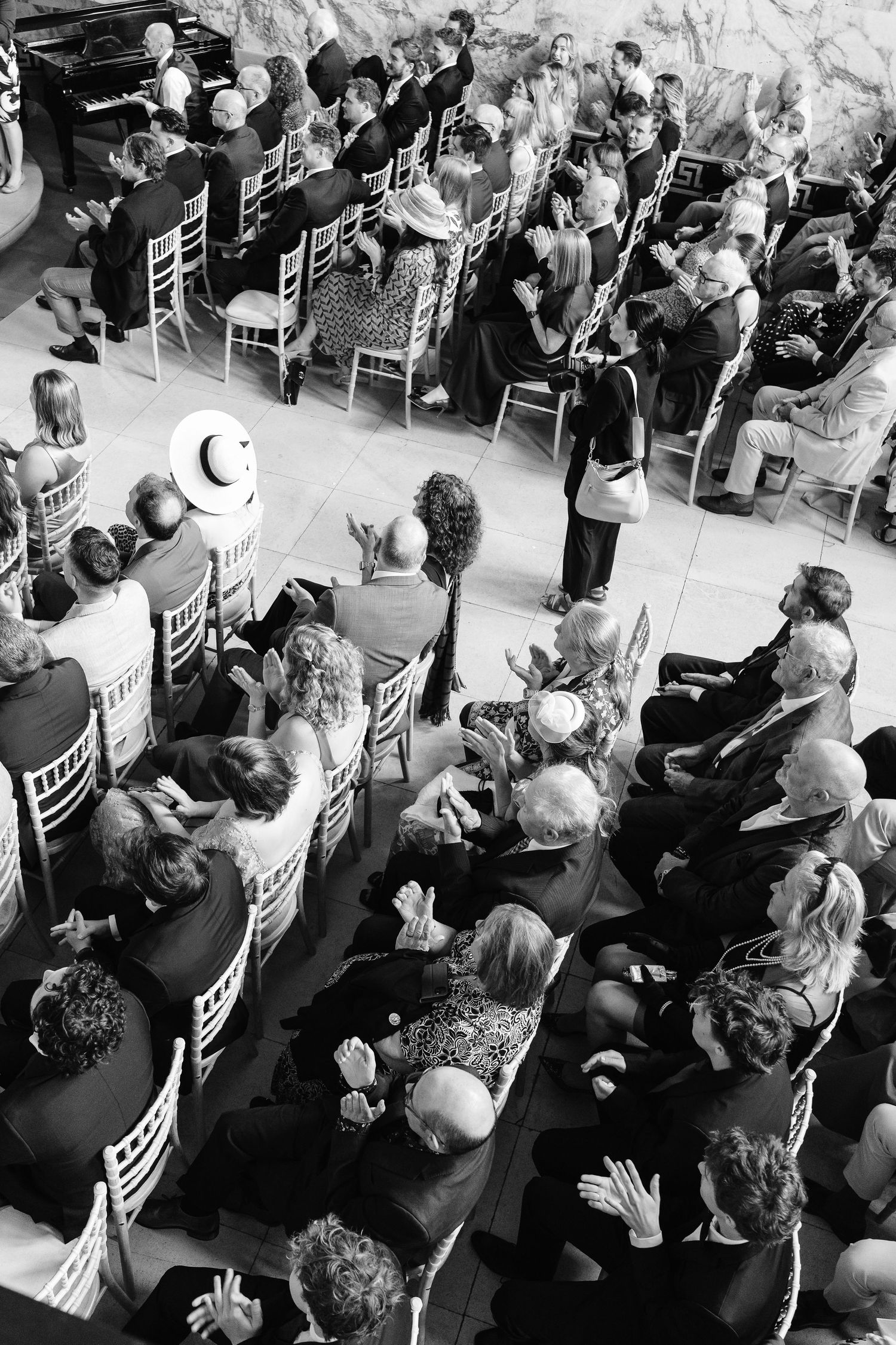 Black and white aerial view of wedding ceremony guests seated in rows of chairs during an indoor celebration.