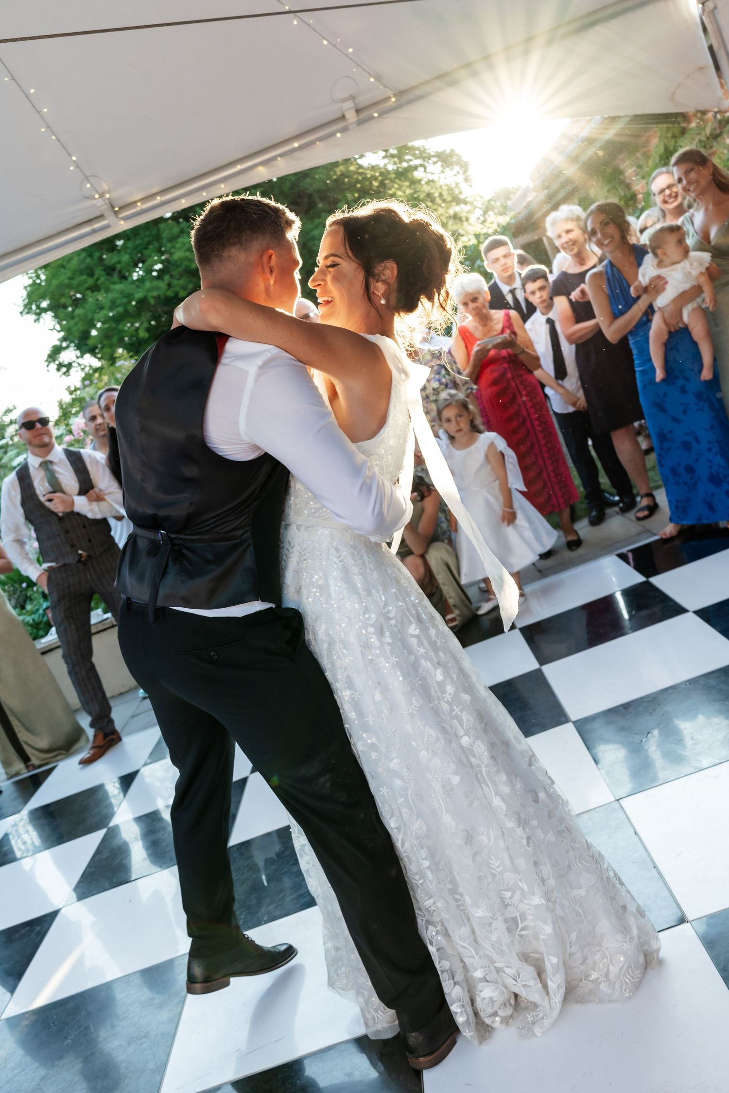 Bride and groom sharing their first dance on a checkered floor under a marquee.